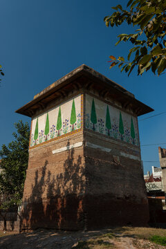 View of Saru wala Maqbra featuring intricate tile work depicting cypress trees and flowers on its upper walls under a clear blue sky in Lahore, Punjab, Pakistan.