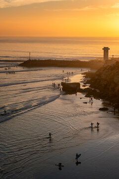 View of surfers in the water at sunset near the pier and lighthouse in Imsouane, Souss-Massa, Morocco.