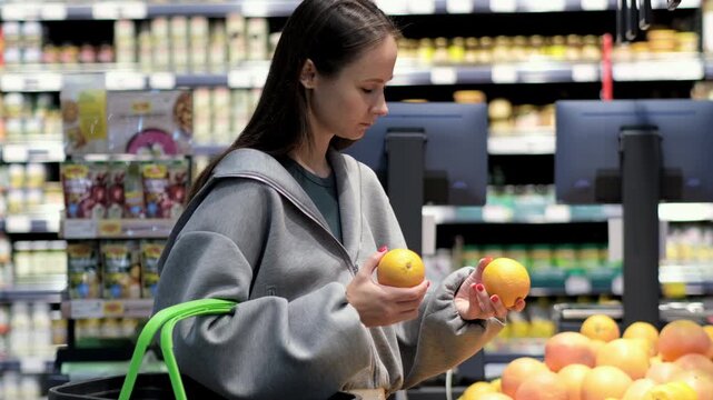 Close-up: a young woman selecting fresh fruit in a supermarket or at a market; a female shopper holding a piece of fresh fruit while shopping.