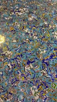 Close-up of decorative blue mosaic tiles featuring floral and botanical motifs arranged in an intricate repeating pattern.