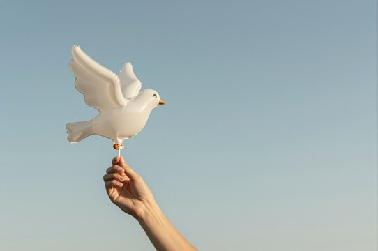 hand holding a white dove balloon against clear blue sky representing peace and freedom