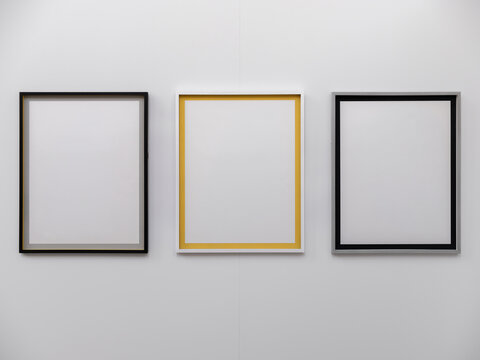 Three empty picture frames in gold, silver and black hang on a gallery wall with copy space.