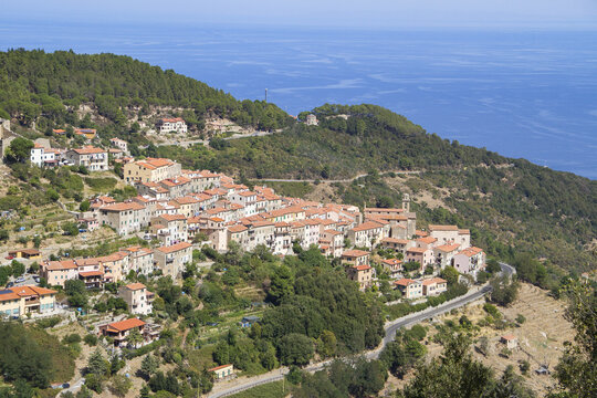 View of the historic village of Marciana nestled on the slopes of Mount Capanne with terracotta rooftops, lush green hills, and the Mediterranean Sea in the background, Elba, Tuscany, Italy.
