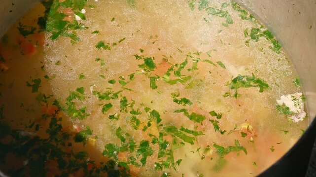 Cooking process of soup with herbs and vegetables in a pot on the stove