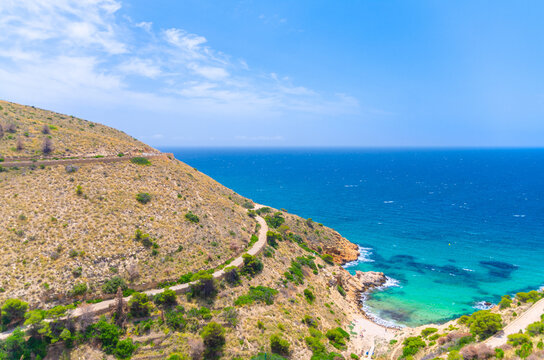 Aerial view of Cala Tio Ximo cove beach Benidorm bay Mediterranean Sea azure water, Costa Blanca coastline coast and mountain road serpentine on hill in Serra Gelada natural park in summer day, Spain