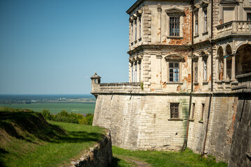 Old castle stands on a hill overlooking a landscape with fields and a distant view of water on a clear day © Stas