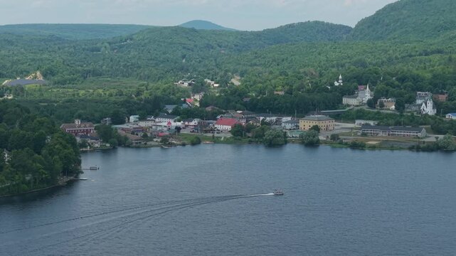 Stationary drone with pontoon boat cruising by the village of Island Pond, Vermont on a summer afternoon