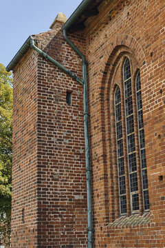 View of St. Catharina Church featuring red brick masonry, a tall arched stained glass window, and a weathered copper downspout in Ribe, Denmark.