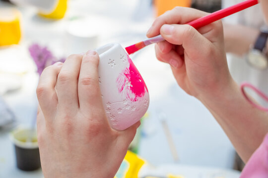 Child hands painting white ceramic mug with pink paint brush
