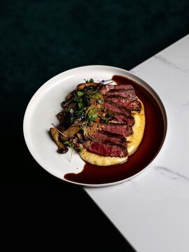 Elegant gourmet steak sliced and beautifully plated with colorful vegetables, rich sauce and refined garnish on a white plate, creating a premium restaurant presentation for culinary concepts.