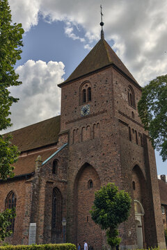 View of St. Catharina Church in Ribe, Denmark, featuring its historic red brick architecture, tall tower, and arched windows under a cloudy sky.
