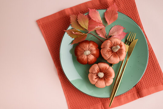 Autumn harvest decor three velvet pumpkins on a plate with golden cutlery and fall leaves