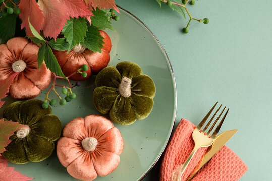 Velvet pumpkins arranged on a plate with golden cutlery and autumn leaves for a festive table setting
