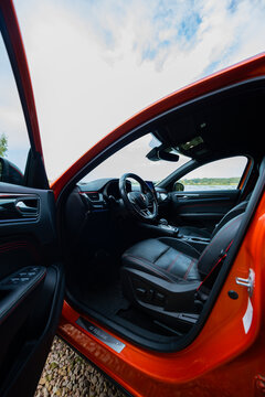 An open driver door reveals leather seats with red stitching, a flat bottom wheel, paddle shifters, and RS Line sills, shot low in daylight to stress coupe SUV form.