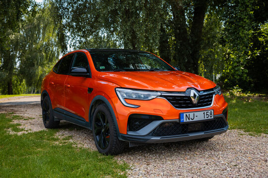 Renault Arkana RS Line coupe SUV in orange parked on a gravel turnout with black alloys, diamond grille, C shaped LED lights, NJ 158 plate, soft daylight, three quarter front view