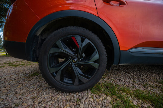 Ground level daylight view shows Renault Arkana RS Line rear quarter, matte black multi spoke alloy, red caliper, orange body, rugged cladding, coupe SUV curves on gravel.