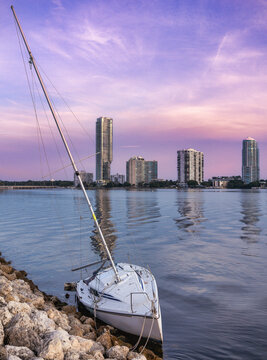 Stranded Sailboat on Rocky Shore with Miami Waterfront Skyline at Twilight