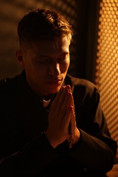 Priest with rosary praying in confessional booth