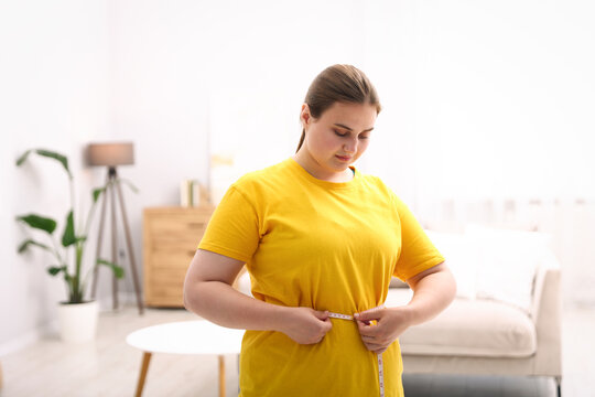 Weight loss. Overweight woman measuring her waist with tape indoors