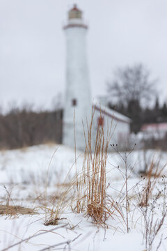 Aerial view of Sturgeon Point Lighthouse surrounded by snow-covered ground and dry winter grass in Harrisville, Michigan, United States.