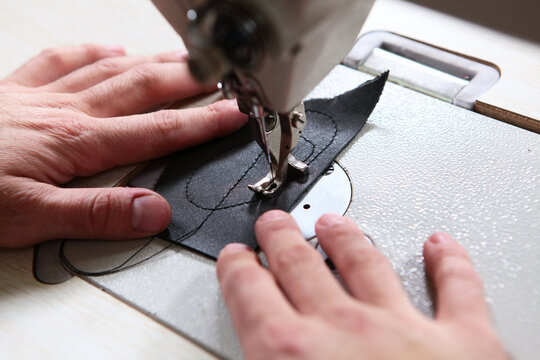 Close-up of master's hands sewing black leather on an industrial sewing machine with guiding template