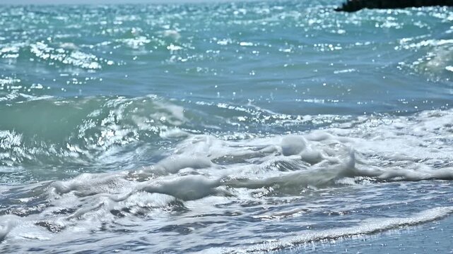 Ocean waves crashing on sandy beach, sunlight reflecting on water surface