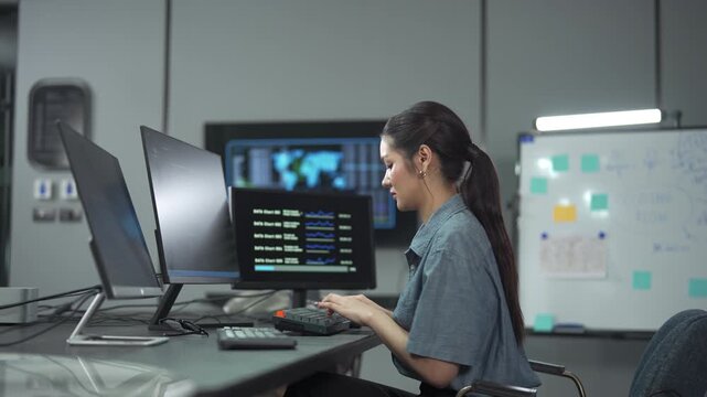 Young female software engineer writing program code on multiple desktop screens in a modern office.