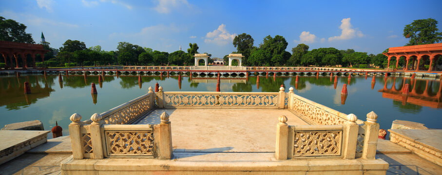 View of the historic Shalamar Gardens featuring a serene reflecting pool, ornate marble pavilion with intricate stone carvings, and lush greenery in Lahore, Punjab, Pakistan.