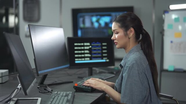 Young female software engineer writing program code on multiple desktop screens in a modern office.