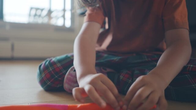 Boy in an orange shirt shaping modelling clay on the living room floor