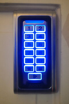 Electronic keypad for home security mounted on a wall with bright blue lights shining from behind the number buttons for nighttime access and easy visibility