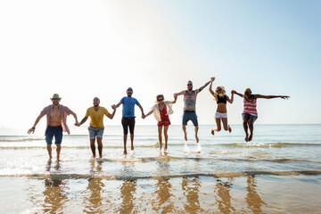 Obraz premium Group of diverse friends joyfully jumping on a sunny beach.