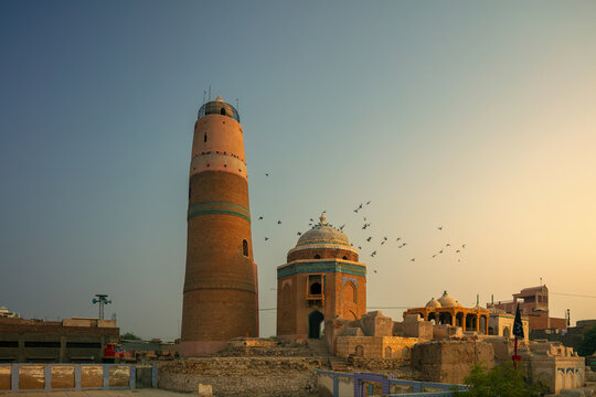 View of the historic Masoom Shah Minara tower and adjacent tomb with birds flying in the sky during golden hour in Sukkur, Sindh, Pakistan.