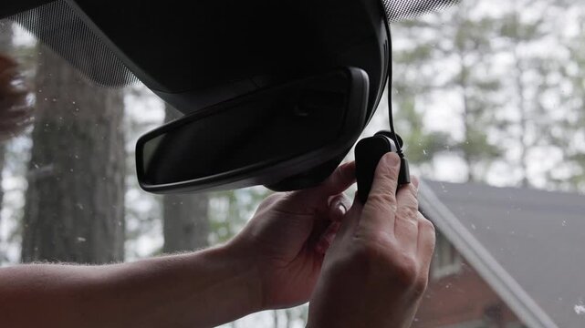 Close-up of a person removing a memory card from a dash camera mounted near the rear-view mirror. Horizontal.