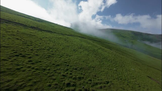 FPV low flight over green hillside with clouds rolling across landscape
