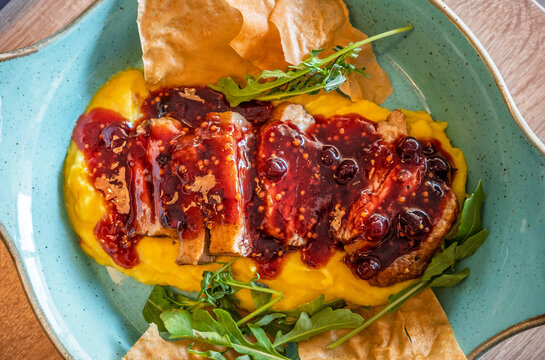 Gourmet roasted pork with berry sauce, golden puree, arugula and crispy chips on turquoise plate, modern restaurant cuisine and fine dining presentation.