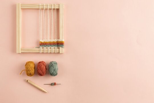 Hand weaving loom craft kit with yarn balls, wooden shuttle and tapestry project on pink background with copy space