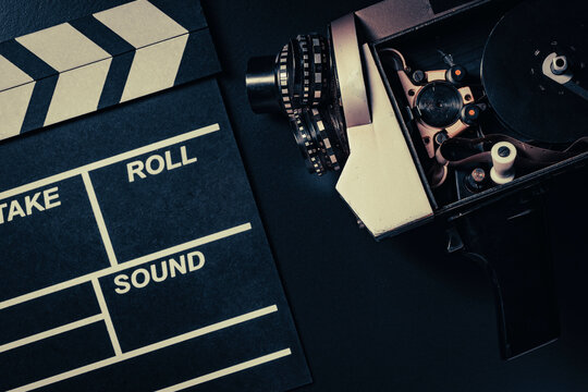 Vintage movie camera and clapperboard on black background, closeup. Top view of an open retro movie camera with film reel next to black movie clapperboard on dark surface