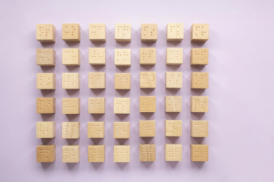A Grid Arrangement of Wooden Cubes Featuring Embossed Tactile Braille Patterns on a Light Purple Background