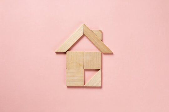 Conceptual house structure formed by natural wooden blocks on a soft pink background, symbolizing home ownership, construction, property investment, and secure living spaces