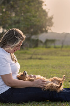 
Young woman sitting on the grass with a dog on her lap, lying belly-up on a sunny day.