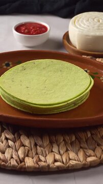 Fresh green spinach or nopal tortillas stack on traditional Mexican clay plate with cheese and salsa