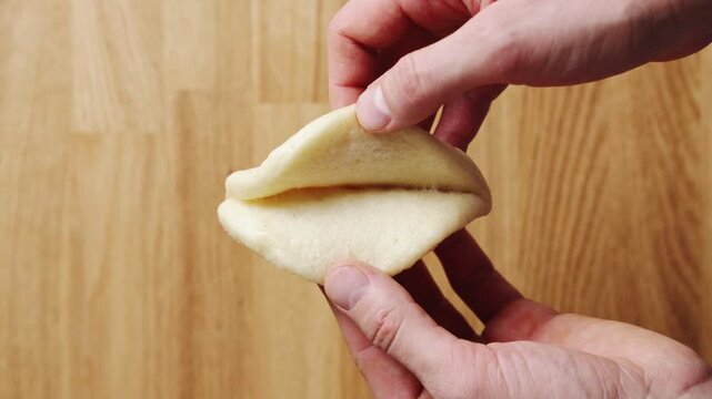 Hands open hot bao bun, revealing soft white centre. Bao bun has fluffy, moist texture after gentle steaming. Bao bun shows proper yeast proofing for light Asian steamed bread and fresh dough quality.