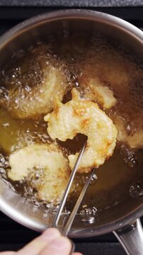 Tweezers lift fried shrimp from hot oil. Fried shrimp has golden crust, crisp batter and juicy seafood centre. Serve fried shrimp in seafood baskets, crispy wraps, pub platters or party snacks.