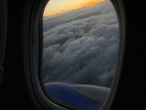 View of clouds from airplane window during sunset over the horizon