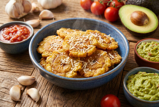 Fried plantain tostones with guacamole and salsa on wood table