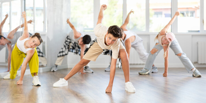 During rehearsal workout, teenage guy dances hip hop with friends against background of large mirror, window. Youth culture, active hobbies, dance subculture