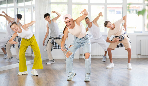 Positive teenage girl training simple hip hop steps in dancehall during workout session in group