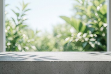 Obraz premium Concrete counter casts leaf shadows before blurred green foliage, bright sky seen through window. Natural outdoor light creates soft bokeh effect, perfect for product display nature themed graphics.