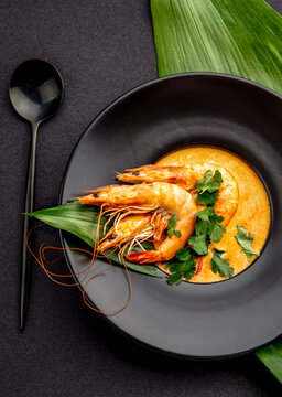 Seafood cream soup with shrimps in black plate, on black background. Top view